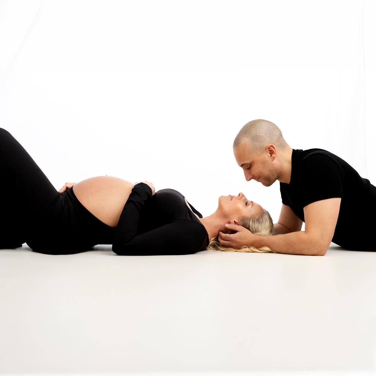 schwangere-Frau-auf-dem-Boden-im-Fotostudio-umarmt-von-ihrem-Partner
